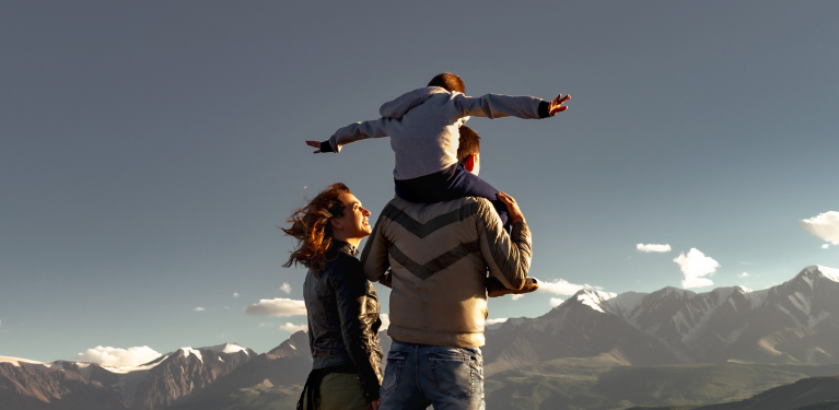 Photo of two adults facing the mountain with a child on one of their shoulders